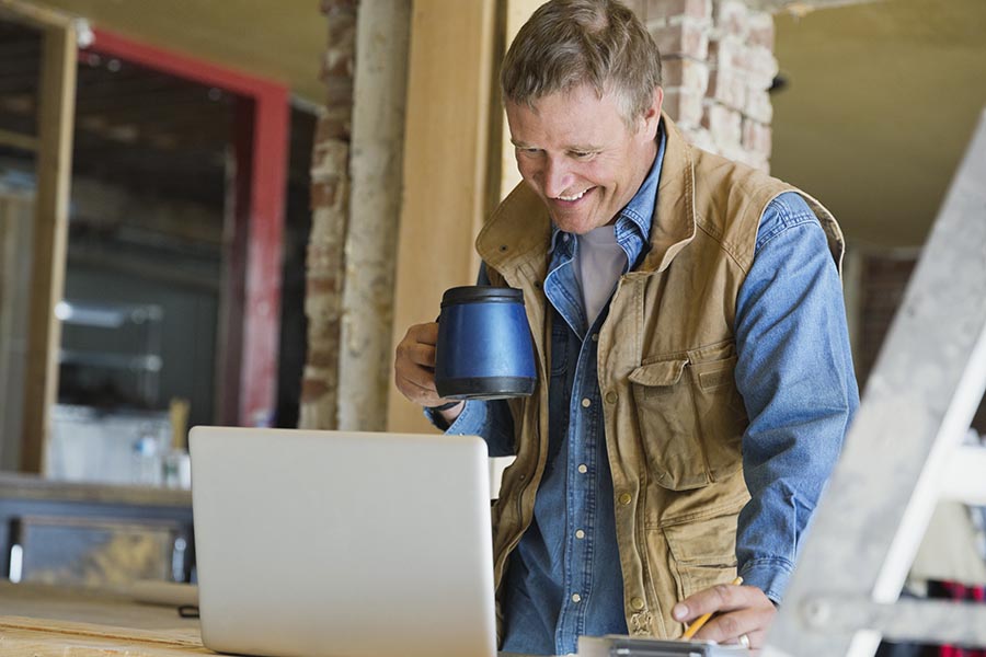 Client Center - Contractor Using a Computer at a Job Site While Drinking Coffee