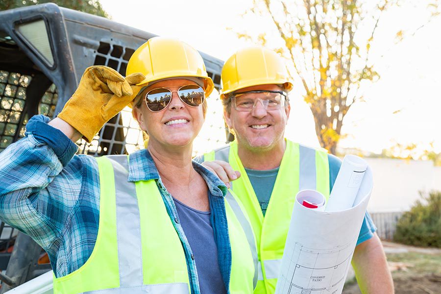 Specialized Business Insurance - Contractors Wearing Reflective Vests and Yellow Hard Hats, Smiling and Holding Blueprints